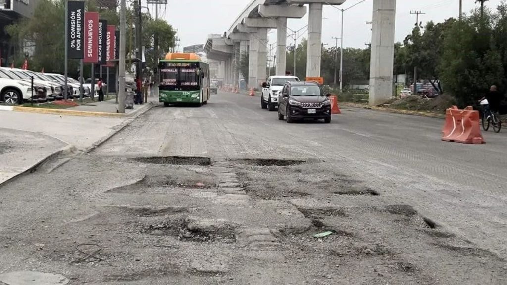 Pothole-filled Urban Road Under Construction with Cones, a Bus and Cars Driving Past, and Elevated Concrete Supports Overhead on the Right Side of the Street. › Regiadísticas