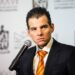 Mike-flores-08may › Regiadísticas Man in a Dark Suit with an Orange Striped Tie Speaks into a Microphone at a Conference or Event. › Regiadísticas